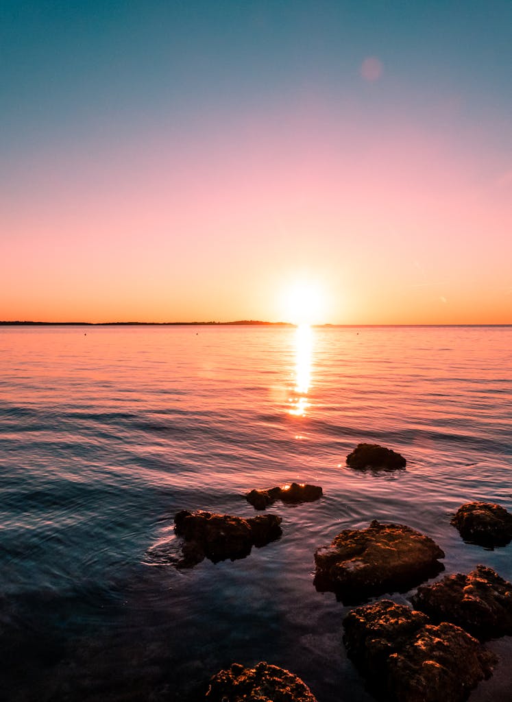 Experience the serene beauty of a sunset in Peroj, overlooking the Adriatic Sea with rocky shores.