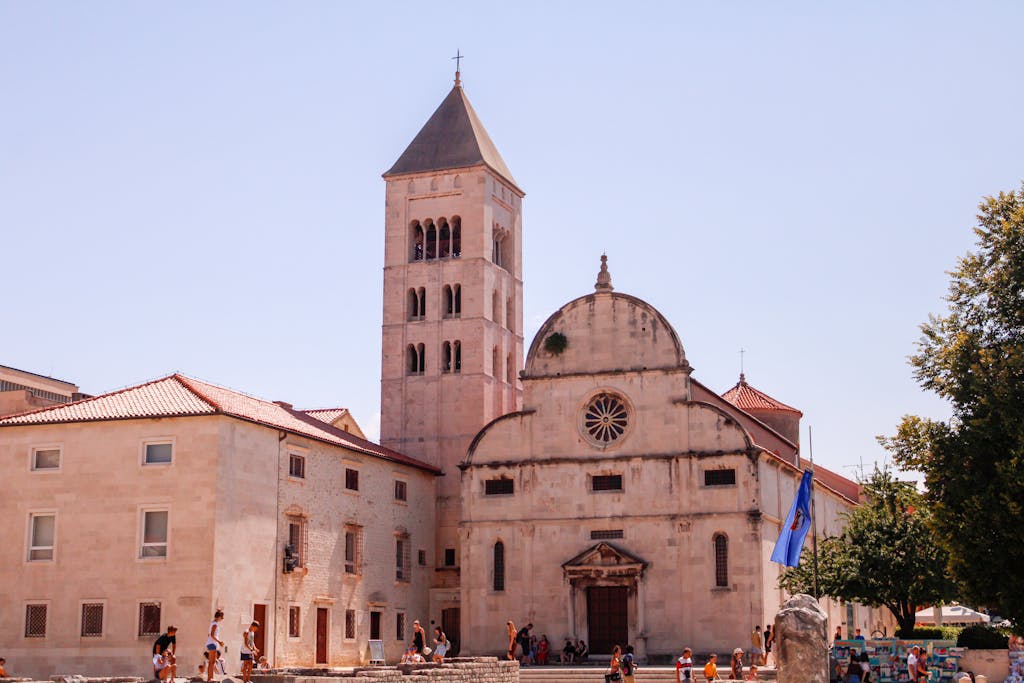 A historic church exterior under a bright summer sky, surrounded by tourists exploring the vibrant square.