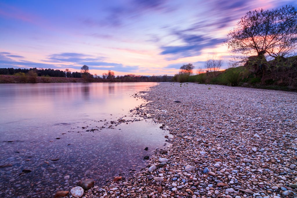 A tranquil scene of a riverbank in Zagreb, Croatia during twilight with a dramatic sky.